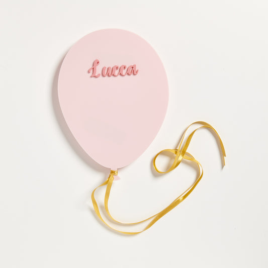 A photo of a party balloon made from 3mm blush pink acylic and topped with the name Lucca in Pastel pink. The balloon also has a gold satin ribbon attached.