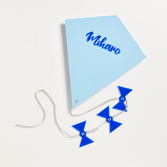 A photo of a kite made from 3mm pastel blue acrylic and topped with the name Miharo  in Blue gloss acrylic. The kite also has a silver satin ribbon and 3 blue acrylic bows attached..