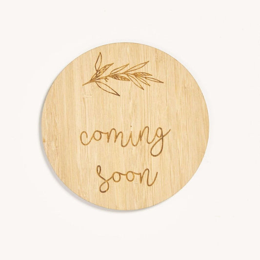 Round wooden sign with 'coming soon' text and leaf design on a white background