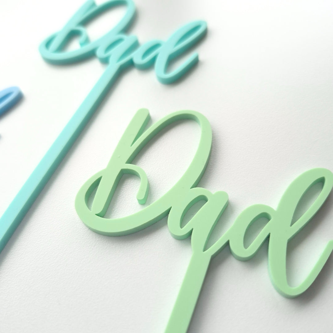 Two 'dad' signs, one in turquoise and one in green, on a white background.